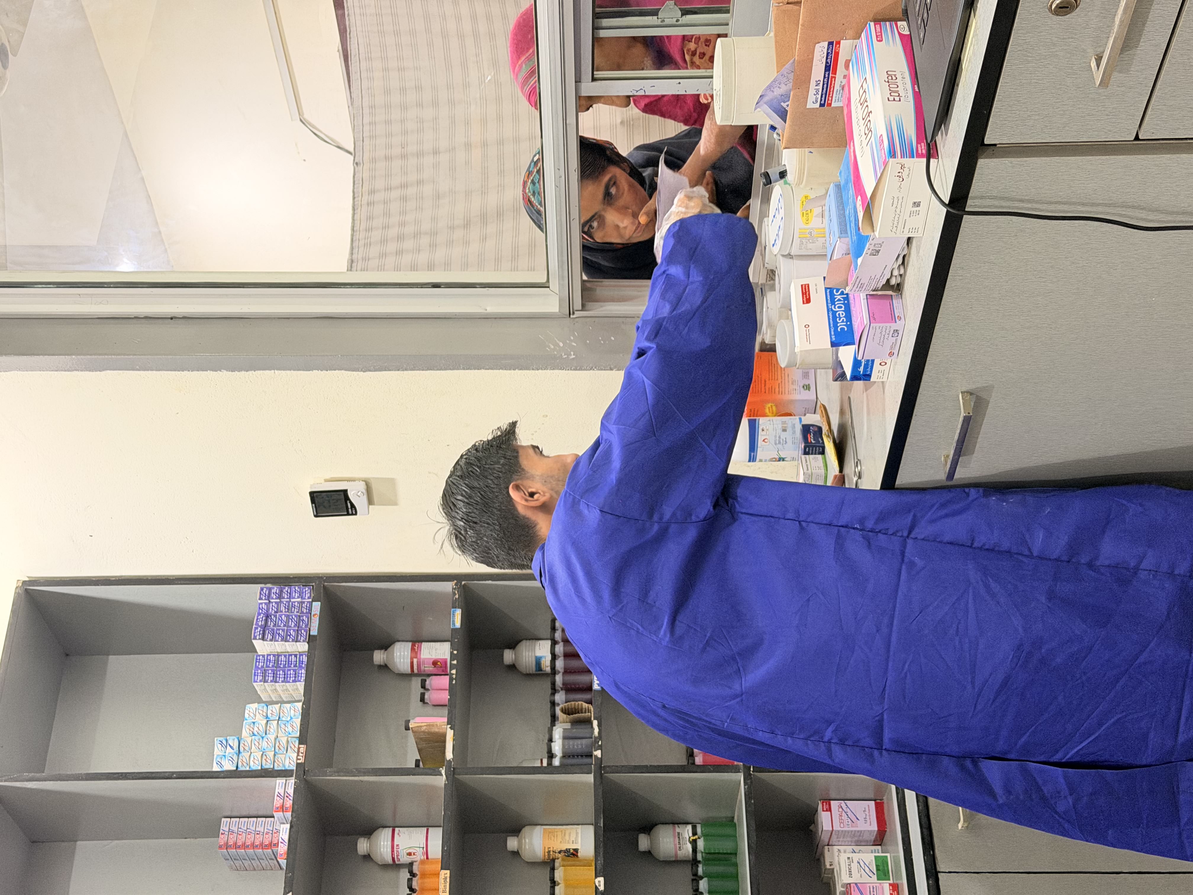 A pharmacist handing medicine through the dispensing window to two women during a routine clinic visit.
